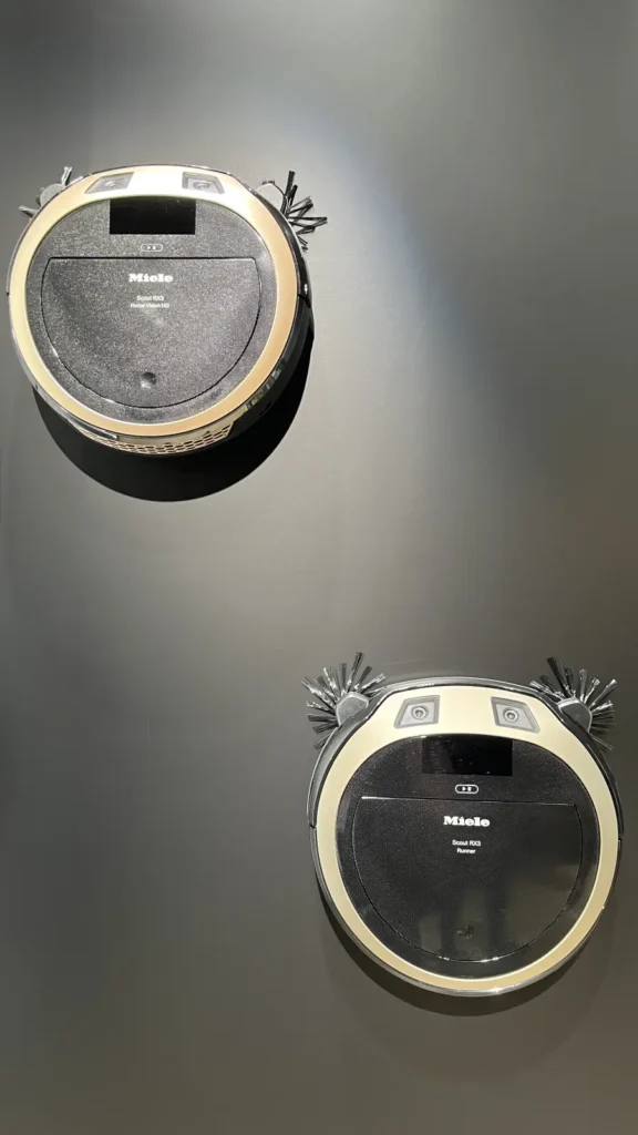 Zwei Miele Scout RX3 Saugroboter als Ausstellungsstücke an einer Messewand